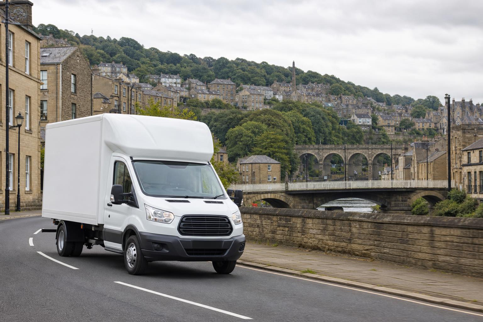 White Luton hire van driving through a riverside town setting in Sowerby Bridge